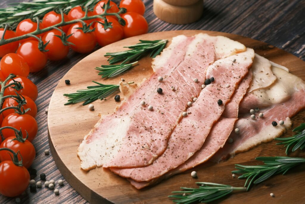 pexels-photo-8395811-8395811 Rustic ham slices with rosemary and cherry tomatoes on wooden board. Perfect for food photography.